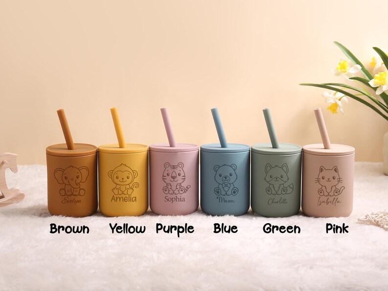 May include: Six colourful silicone cups with straws, each with a different animal design and name. The colours are brown, yellow, purple, blue, green, and pink. These cups are designed for children.