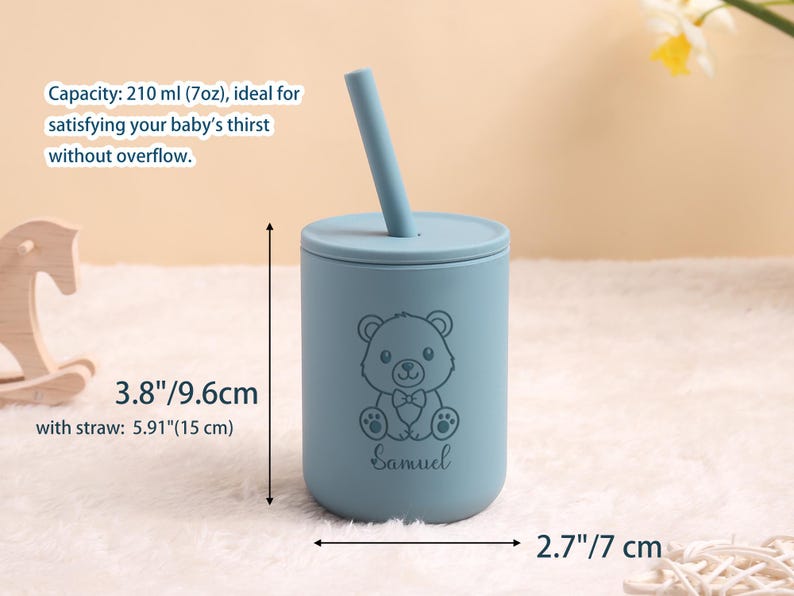 May include: A pale blue baby cup with a lid and straw. The cup has a bear illustration and the name "Samuel". It measures 9.6 cm tall and 7 cm wide. With the straw, it is 15 cm tall. Holds 210 ml. A cute and practical item for babies.