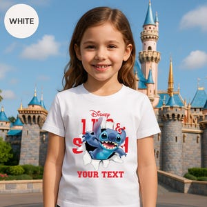 A young girl wearing a white t-shirt with a Disney character printed on it, standing in front of a castle.