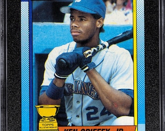 Peut inclure: Carte de baseball Topps 1990 classée, représentant Ken Griffey Jr. en uniforme des Mariners. La carte est encadrée dans un support noir avec une note de 8,5. La conception de la carte comprend le logo des Mariners, le nom du joueur et le logo Topps.