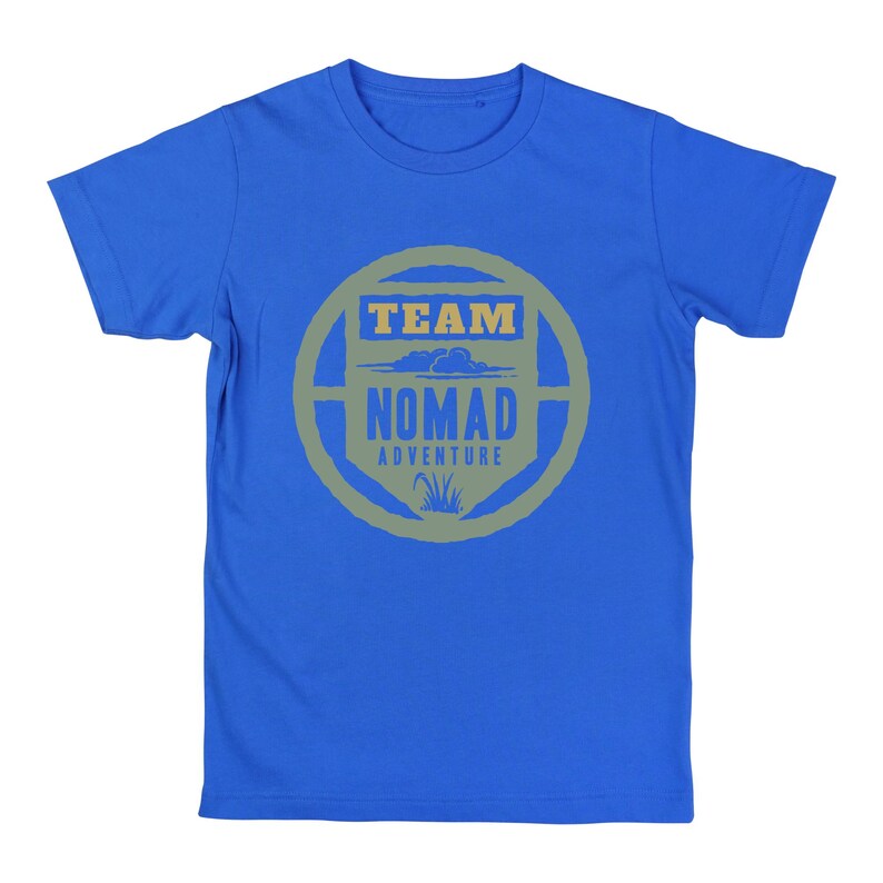 May include: A blue t-shirt with a circular graphic in shades of gray and green. The graphic reads "TEAM NOMAD ADVENTURE" with a cloud and grass design. The shirt is made of a soft material.