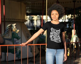 May include: Black crew neck t-shirt with the text "I'm not antisocial, society is anti-me" in white. The person is wearing blue jeans. The background includes a carousel with horses.