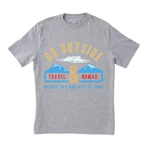 May include: A heather gray t-shirt with a graphic design. The design includes the words "GO OUTSIDE" in gold, with a mountain and cloud illustration, and the words "TRAVEL & NOMAD" in blue and red. The text "BEFORE YOU RUN OUT OF TIME" is in blue.
