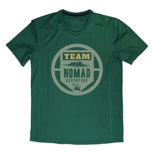 May include: A dark green athletic t-shirt with a crew neck and short sleeves. The shirt features a circular graphic with the words "TEAM NOMAD ADVENTURE" in a light tan color. The graphic includes a cloud and grass design.