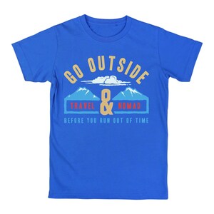 May include: Blue t-shirt with a graphic design. The design includes the words "GO OUTSIDE" in gold, with a cloud and mountain illustration. Below the mountains are the words "TRAVEL & NOMAD" and the phrase "BEFORE YOU RUN OUT OF TIME".