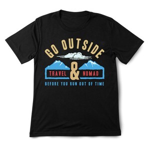 May include: Black t-shirt with a graphic design. The design features the words "GO OUTSIDE" above a mountain scene with the words "TRAVEL & NOMAD" and the phrase "BEFORE YOU RUN OUT OF TIME".