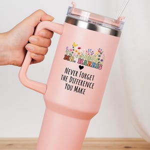 May include: A pink insulated tumbler with a handle, a clear lid, and a straw. The tumbler has the text "Mr. Harris Never Forget The Difference You Make" with a floral design. A great gift for a teacher.