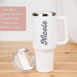 May include: White 40oz insulated tumbler with a handle and a silver rim. The name "Nicole" is printed in gray script on the side. The lid and straw are visible. The text on the image says the tumbler is made from food grade stainless steel.