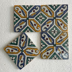 Può includere: Una collezione di piastrelle in ceramica colorate con un motivo geometrico ripetuto. Il design presenta accenti blu, gialli, verdi e rossi. Una piastrella è a forma di diamante, le altre sono quadrate.