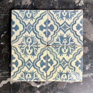 Puede incluir: Cuatro baldosas de cerámica cuadradas con un patrón floral azul y crema repetido. Las baldosas están dispuestas juntas, mostrando el intrincado diseño. El patrón presenta elementos florales y geométricos estilizados.