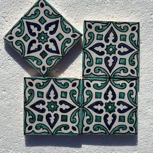 Peut inclure: Quatre carreaux de céramique carrés sur fond blanc. Chaque carreau présente un motif répétitif de motifs floraux et géométriques turquoise, bleu foncé et noirs. Un carreau est tourné en losange.