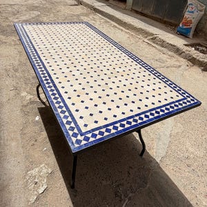 May include: A rectangular table featuring a mosaic tile top with a geometric pattern of cream-colored octagons and small dark blue squares, bordered by a blue and white diamond motif, supported by four thin black metal legs.