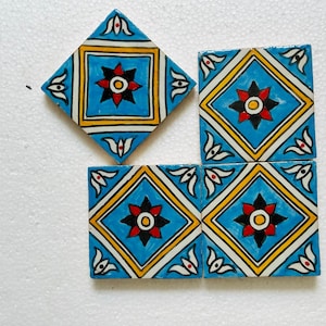 Pode incluir: Quatro azulejos de cerâmica com um design pintado à mão. Os azulejos são quadrados e em forma de diamante, com um fundo azul claro e uma borda amarela e branca. Cada azulejo tem um motivo floral central em vermelho, preto e amarelo.
