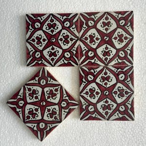 Może przedstawiać: Cztery kwadratowe i jedna dekoracyjna płytka w kształcie rombu. Każda płytka ma powtarzający się wzór białych i bordowych kwiatowych i geometrycznych wzorów. Płytki są ułożone na białej powierzchni.