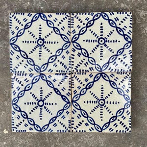 May include: Four square ceramic tiles with a white background and a repeating blue geometric pattern. The design features a central starburst surrounded by a diamond-shaped chain of connected ovals and dotted lines.