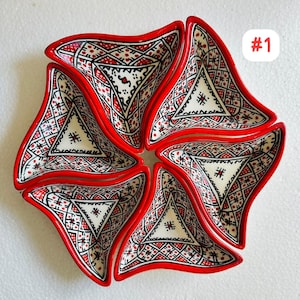 以下が含まれることがあります： 花のような形に配置された、6つのセラミック製サービングディッシュのセット。各皿は赤い縁と、幾何学的な黒と赤の模様が入った白い内側を持っています。「#1」の文字が右上隅にあります。