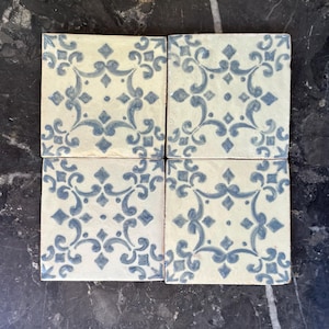 Puede incluir: Cuatro baldosas de cerámica cuadradas con fondo crema y un patrón floral azul repetitivo. Las baldosas están dispuestas en una formación cuadrada, mostrando el intrincado diseño. Las baldosas son adecuadas para la decoración del hogar.