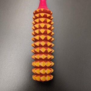 May include: A handcrafted wooden massage tool with a red and yellow geometric design. The tool has a cylindrical shape with a series of diamond-shaped protrusions. The top is painted red, and the base is a natural wood color.