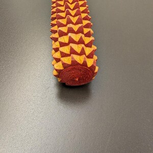 May include: A wooden massage tool with a textured surface. The tool is primarily red with yellow accents, and has a rounded base. The massage tool is designed to be held in the hand and used to massage muscles.
