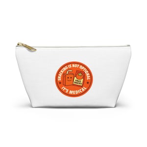 Könnte beinhalten: Weiße Canvas-Tasche mit goldenem Reißverschluss und einem kreisförmigen orangefarbenen Aufdruck. Der Aufdruck lautet "Snacking is not optional, it's medical" und zeigt eine Saftbox und eine Obst-Snack-Packung.