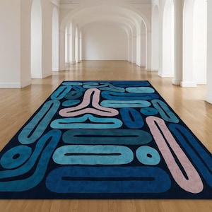 Peut inclure: Un tapis rectangulaire avec un fond bleu foncé et des formes abstraites en différentes nuances de bleu et de rose. Les formes comprennent des ovales, des cercles et un motif stylisé à trois branches. Le tapis est posé sur un sol en bois.