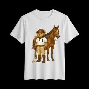 May include: White t-shirt with a cartoon image of a teddy bear in polo gear, standing beside a brown horse. The bear is wearing a polo shirt with the number 1, khaki trousers, and a brown hat. The horse has a saddle and bridle.