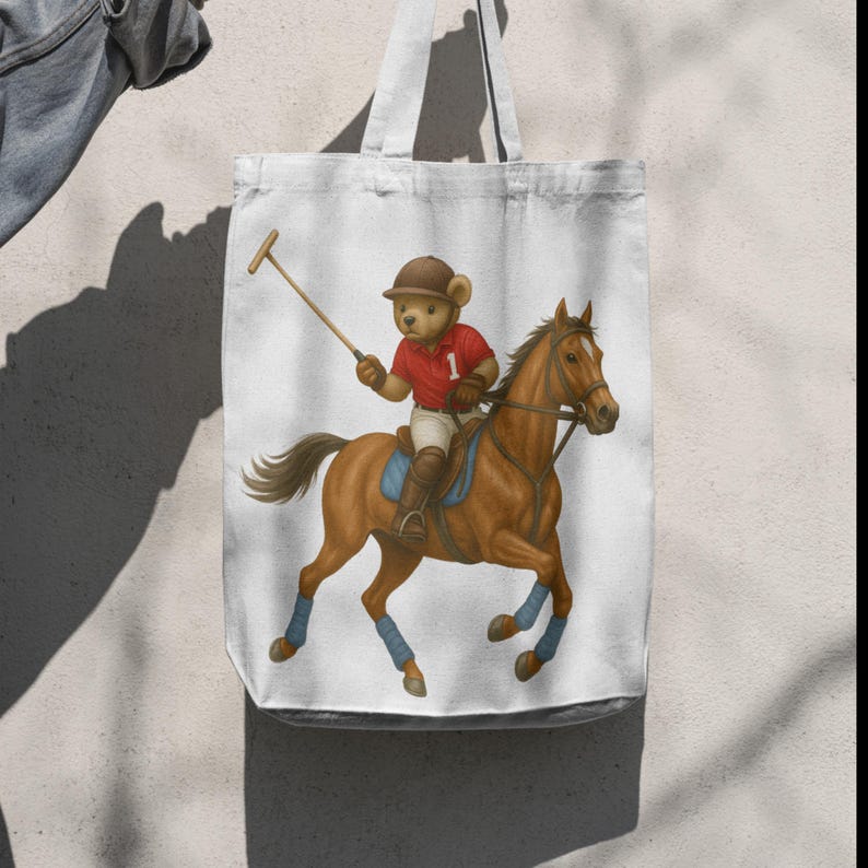 May include: White tote bag with a polo-playing teddy bear on a brown horse. The bear is dressed in a red polo shirt with the number 1, a brown helmet, and blue leg wraps. The horse is depicted in motion, with a polo mallet in the bear's hand.