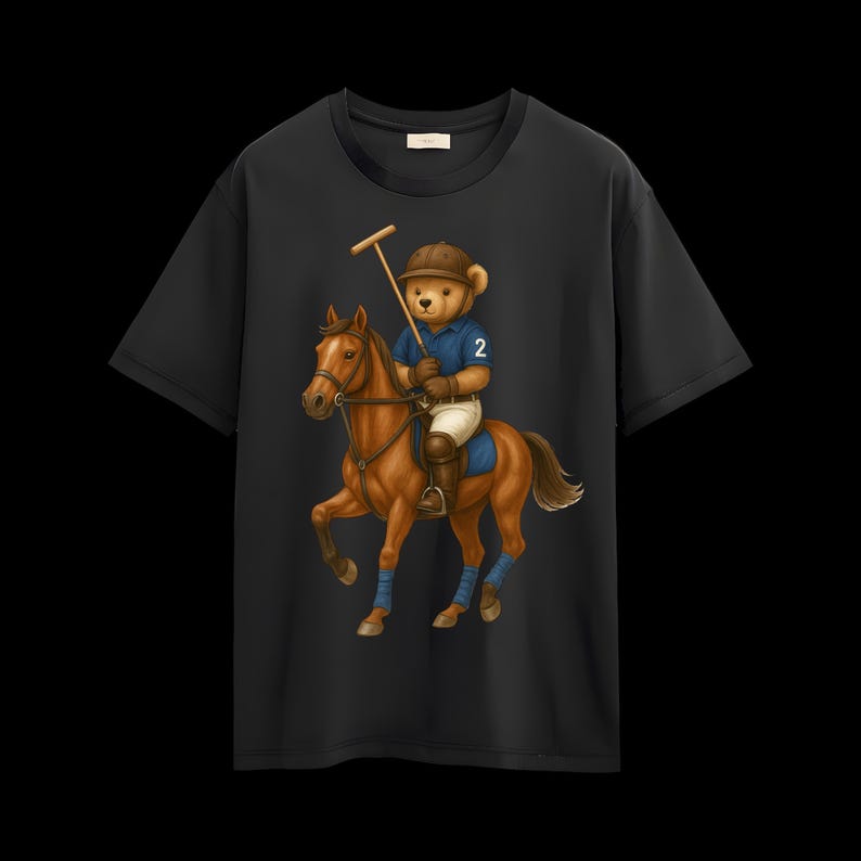 May include: Black t-shirt with a cartoon bear playing polo on a brown horse. The bear is wearing a blue polo shirt with the number 2, a brown helmet, and white trousers. The horse has blue leg wraps and a brown saddle.