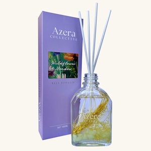 May include: A clear glass reed diffuser bottle with white reeds and yellow botanicals, next to a purple box. The box reads "Azera Collective" and "Wildflower Meadow" with a floral image. The bottle contains 100ml of liquid.