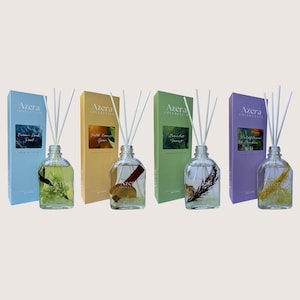 May include: Four reed diffusers with glass bottles and white reeds. Each bottle contains a different botanical element and is paired with a coloured box. The boxes are blue, yellow, green, and purple, each with the "Azera Collective" logo.