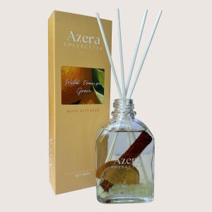 May include: A reed diffuser set featuring a clear glass bottle with white reeds, a cinnamon stick, and an orange slice. The accompanying gold box displays "Azera Collective" and "Wild Orange Grove". The bottle contains 100ml of liquid.