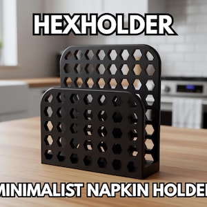 May include: Black minimalist napkin holder with a honeycomb design. The text "HEXHOLDER" and "MINIMALIST NAPKIN HOLDER" are displayed on the image. The holder is made of a solid material and sits on a wooden surface.