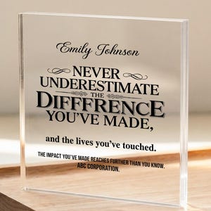 May include: A clear acrylic plaque with black text, including the name "Emily Johnson" and the quote "Never underestimate the difference you've made." The plaque sits on a wooden tray with a laptop and framed picture in the background.