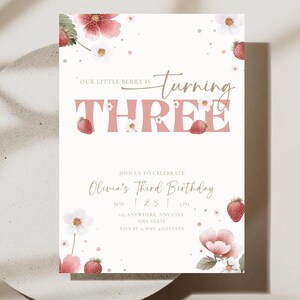 May include: A cream-colored birthday invitation with a strawberry theme. The text "Our Little Berry is Turning Three" is displayed in pink and gold. The invitation includes details for Olivia's third birthday, with floral and strawberry illustrations.