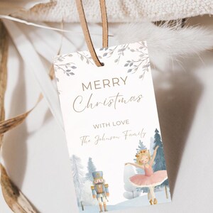 Könnte beinhalten: Ein rechteckiges Weihnachtsgeschenkanhänger mit den Worten "MERRY Christmas" und "WITH LOVE" in eleganter Schrift gedruckt. Das Etikett zeigt eine Aquarellillustration einer Ballerina, eines Nussknackers und Winterbäumen. Ein Lederband ist befestigt.