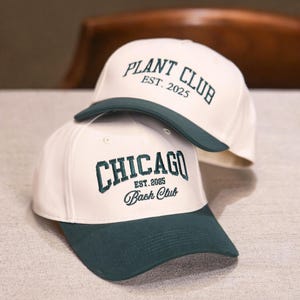 May include: Two baseball caps with white crowns and dark green peaks. One cap features "PLANT CLUB EST. 2025" embroidered in dark green. The other cap has "CHICAGO EST. 2035 Bach Club" embroidered in dark green.
