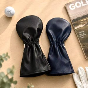 May include: Two golf club head covers, one black and one navy blue, with white accents. A golf ball and a magazine with the text "GOLF" are also visible. The magazine's cover reads "The Best Gear for Your Best Game."