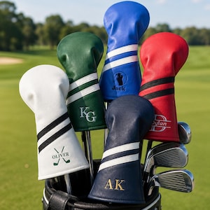 May include: A golf bag filled with golf clubs, each with a personalized head cover. The covers are in various colors, including white, green, blue, red, and navy, with white stripes and initials or names. The background is a green golf course.
