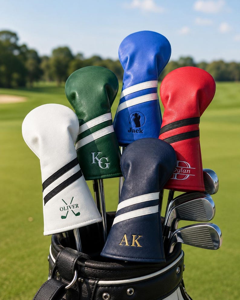May include: A golf bag filled with golf clubs, each with a personalized head cover. The covers are in various colors, including white, green, blue, red, and navy, with white stripes and initials or names. The background is a green golf course.