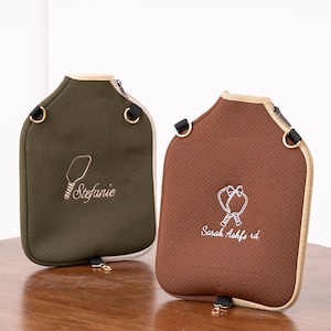 May include: Two water bottle carriers in olive green and brown, each with a zipper closure and a beige trim. The olive green carrier has the name "Stefanie" embroidered in white, and the brown carrier has "Sarah Ashford" embroidered in white.