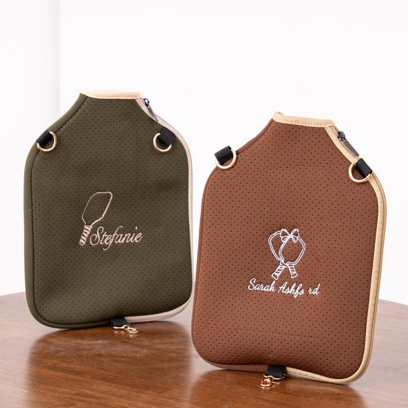 May include: Two water bottle carriers in olive green and brown, each with a zipper closure and a beige trim. The olive green carrier has the name "Stefanie" embroidered in white, and the brown carrier has "Sarah Ashford" embroidered in white.