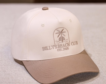 Puede incluir: Gorra de béisbol con corona blanca y visera beige. La gorra presenta un logotipo bordado con una palmera y el texto "BILLY'S BEACH CLUB EST. 2025". La gorra tiene una visera curva y un botón en la parte superior.