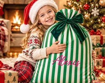 May include: A large fabric gift sack featuring vertical green and white stripes, topped with a dark green velvet bow. The name Alexis is embroidered in bright pink script on the front of the sack. The sack is made of a smooth, satin-like material.