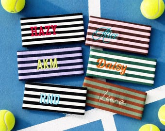 Puede incluir: Seis cintas para la cabeza rectangulares de tela con rayas horizontales de varios colores, cada una con nombres o iniciales bordados como Hazy, Alice, AKM, Daisy, RND y Linna, dispuestas alrededor de cuatro pelotas de tenis amarillas en una pista azul.