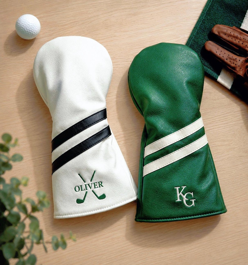 May include: Two golf club head covers, one white with black stripes and the name "OLIVER", the other green with white stripes and the initials "KG". A golf ball, towel, and gloves are also visible.