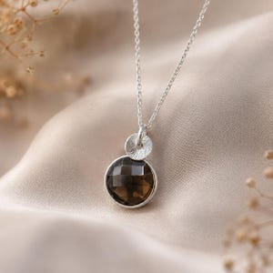 May include: A silver necklace featuring a faceted, dark brown gemstone pendant. The pendant is round and set in a silver bezel, with a textured silver accent above. The chain is delicate and silver.