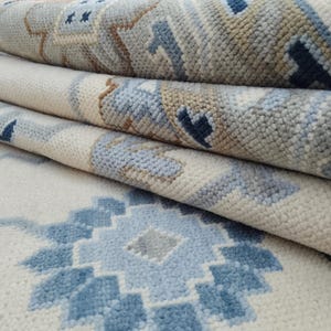 以下が含まれることがあります： 幾何学模様のロールカーペットのクローズアップ。カーペットは、クリーム色の背景に青、グレー、茶色の幾何学模様が特徴です。カーペットは、質感のある素材で作られています。