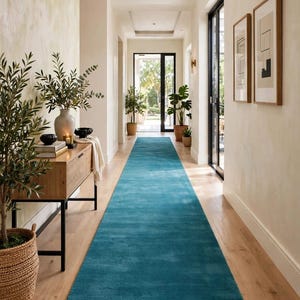 May include: A long, rectangular, solid teal runner rug with a soft, plush texture positioned in a hallway. The rug features the text AdeebaArtRug printed in white near the bottom edge. The hallway has light wood flooring and white walls.