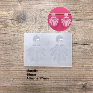 May include: Pink and purple seashell earrings displayed on a pink circle, with a clear silicone mould below. The earrings are made of layered clay. The mould has the text "Marella 45mm Attache 17mm".