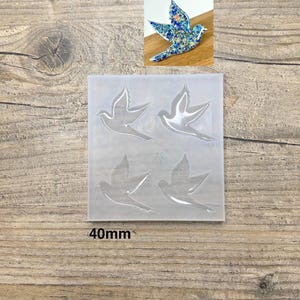 Peut inclure: Un moule en silicone transparent avec quatre formes de colombe, chacune d'environ 40 mm. Un exemple de colombe est présenté dans le coin supérieur droit, avec un motif bleu et floral. Le moule est destiné à la création artisanale.